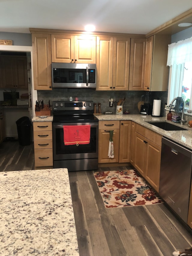 kitchen with stainless steel appliances, sink, light stone counters, dark hardwood / wood-style floors, and backsplash