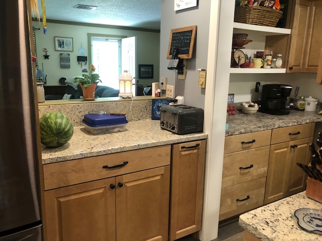 kitchen featuring ornamental molding, a textured ceiling, stainless steel fridge, and light stone counters