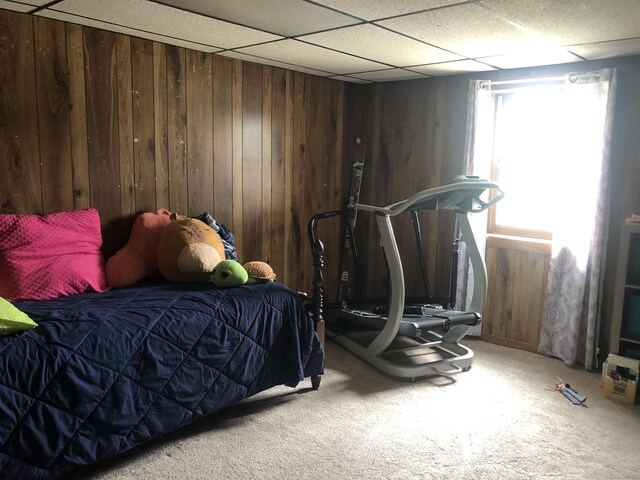 carpeted bedroom featuring wooden walls and a drop ceiling