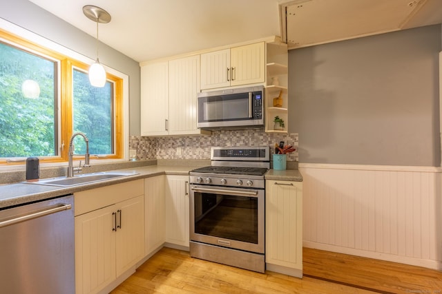 kitchen with sink, white cabinetry, light hardwood / wood-style flooring, hanging light fixtures, and stainless steel appliances