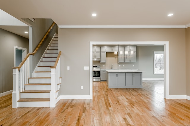 unfurnished living room featuring ornamental molding, sink, and light wood-type flooring