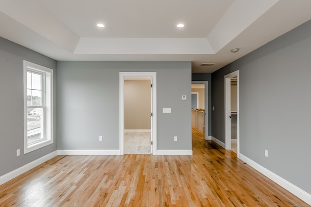 unfurnished bedroom with a raised ceiling, a spacious closet, a closet, and light wood-type flooring