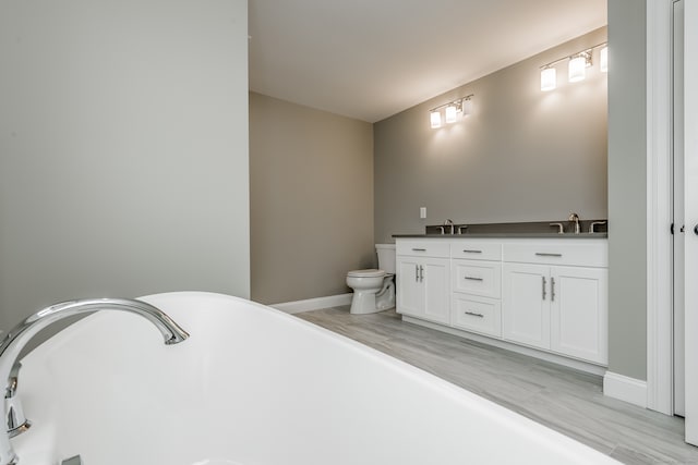 bathroom with a washtub, hardwood / wood-style flooring, toilet, and double sink