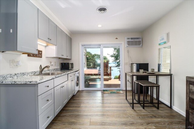 kitchen featuring sink, light stone counters, dark hardwood / wood-style flooring, an AC wall unit, and washer / dryer