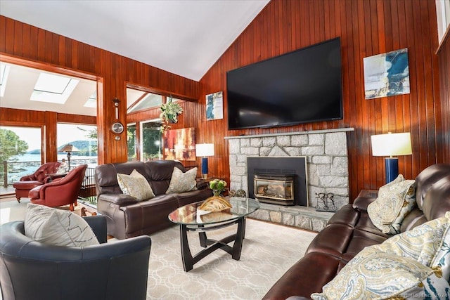 living room featuring a stone fireplace, wood walls, and vaulted ceiling with skylight