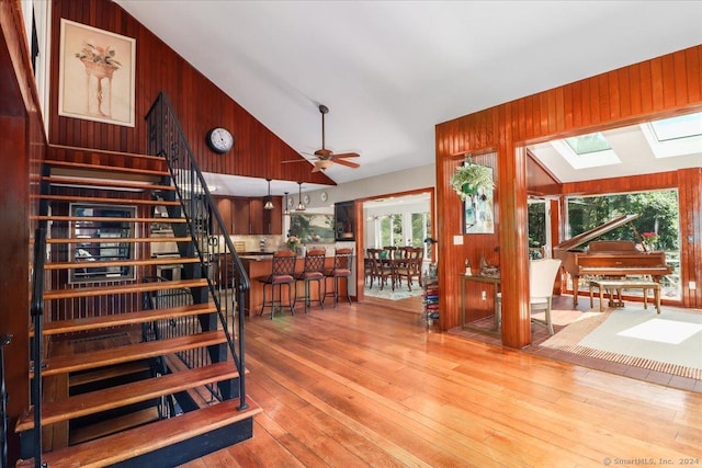 staircase with vaulted ceiling with skylight, ceiling fan, wood walls, and wood-type flooring