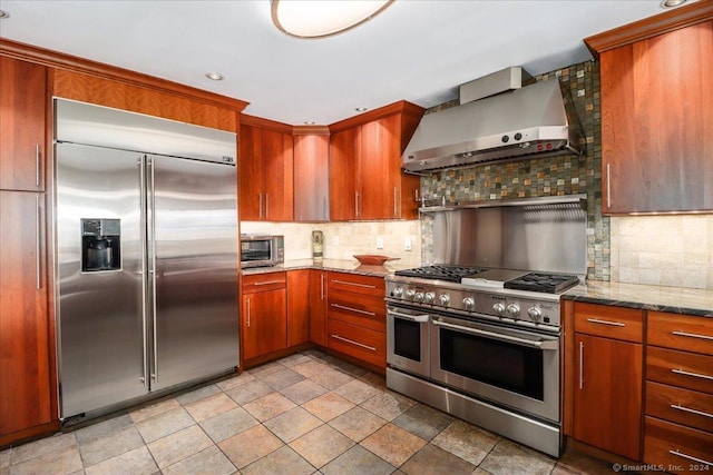 kitchen featuring decorative backsplash, wall chimney exhaust hood, light stone countertops, and premium appliances