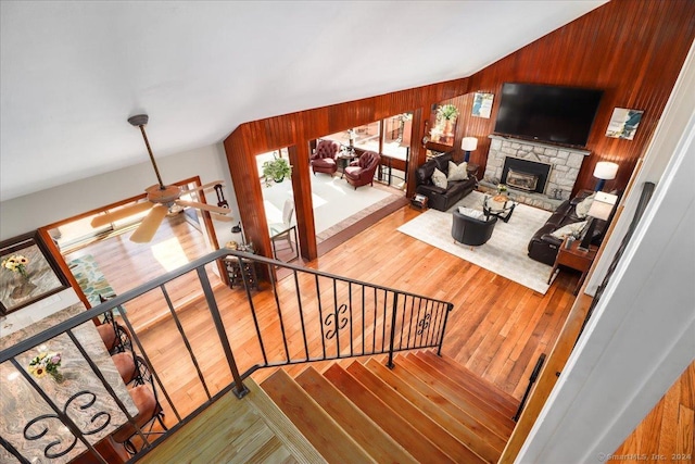 staircase featuring hardwood / wood-style floors, a stone fireplace, ceiling fan, and wooden walls