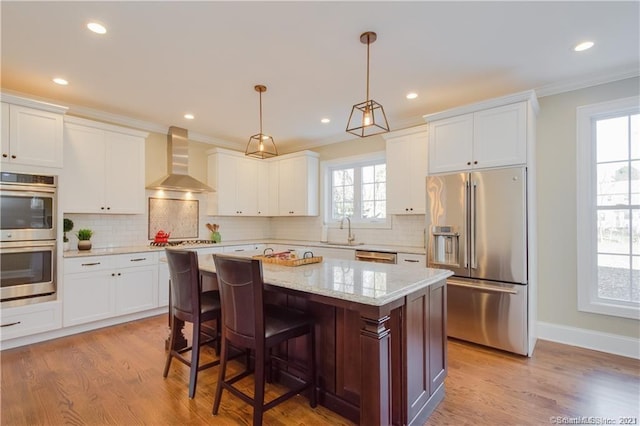 kitchen featuring appliances with stainless steel finishes, wall chimney range hood, backsplash, a kitchen island, and light wood-type flooring