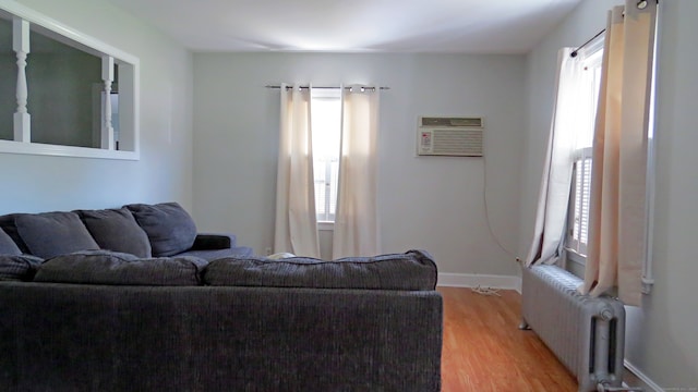 living room with radiator heating unit, a wall mounted air conditioner, and light wood-type flooring