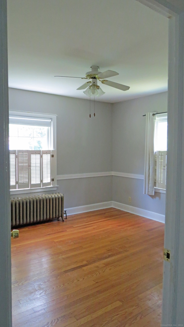 unfurnished room with ceiling fan, hardwood / wood-style flooring, radiator, and plenty of natural light