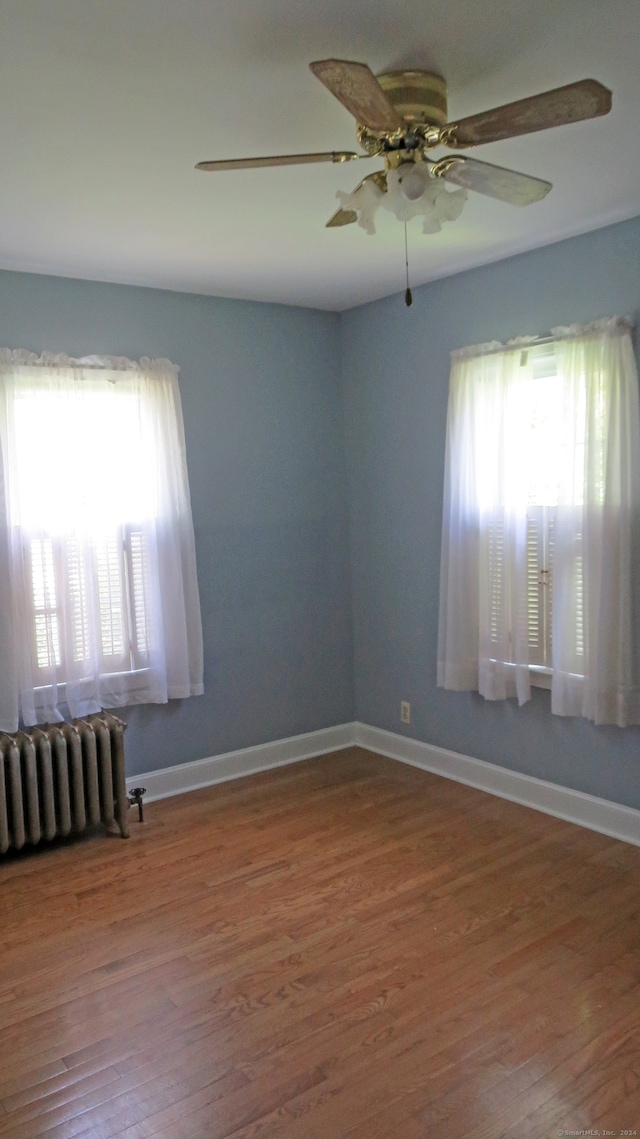 empty room featuring hardwood / wood-style flooring, radiator, and ceiling fan