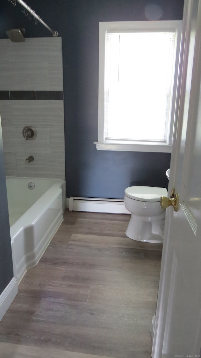 bathroom featuring toilet, tiled shower / bath combo, baseboard heating, hardwood / wood-style floors, and plenty of natural light