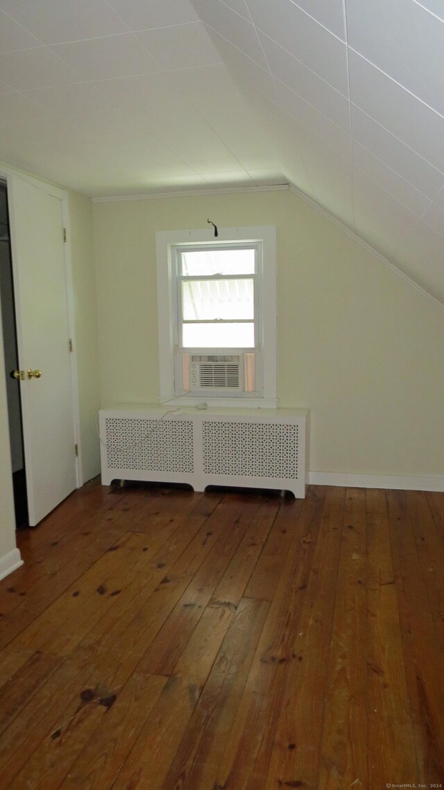 additional living space with wood-type flooring, vaulted ceiling, cooling unit, and radiator heating unit