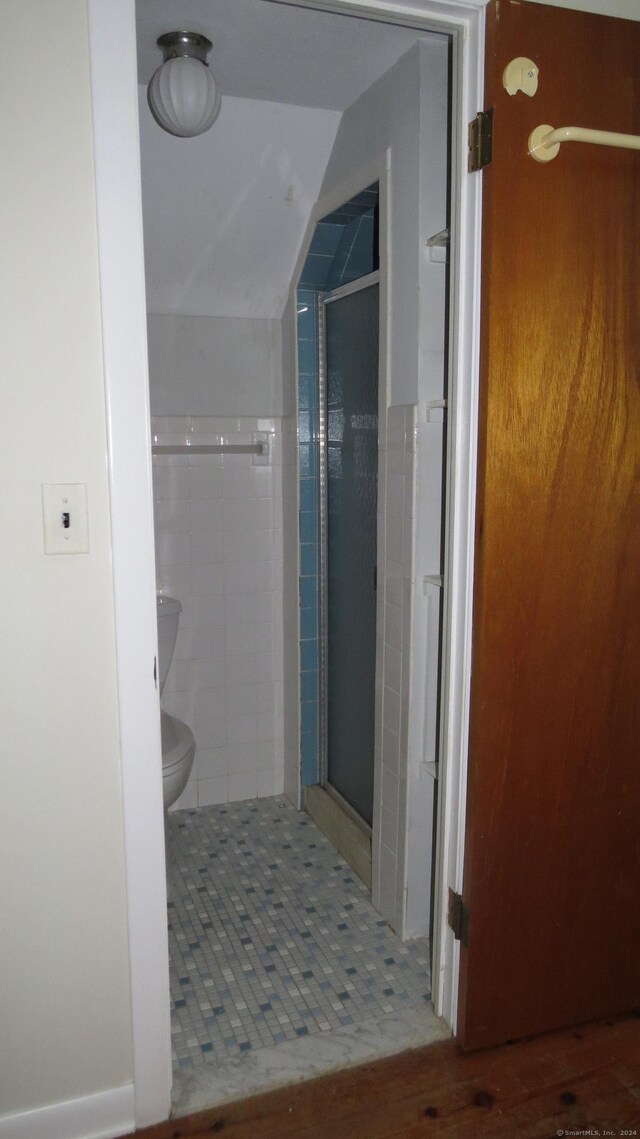 bathroom featuring a shower with shower door, toilet, and tile patterned floors