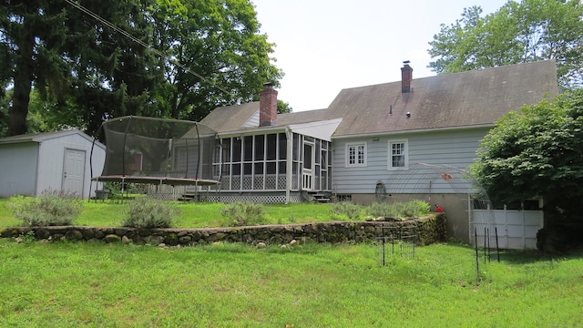 back of property featuring a trampoline, a sunroom, a lawn, and a shed