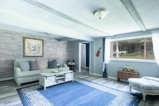 living area with an accent wall, beam ceiling, a textured ceiling, and wood finished floors