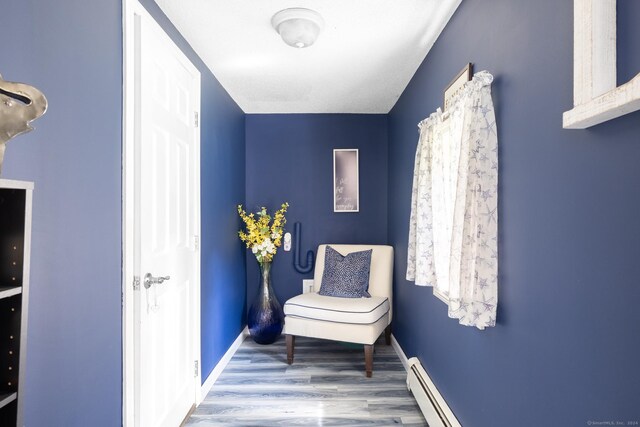 sitting room with a baseboard heating unit, wood finished floors, and baseboards