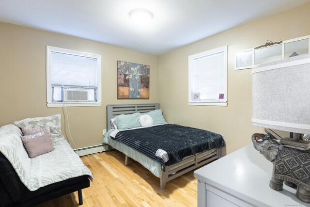 bedroom with light wood-type flooring, a baseboard heating unit, and cooling unit