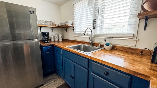 kitchen with stainless steel fridge, sink, blue cabinetry, and wooden counters