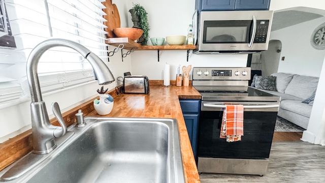 kitchen featuring wood counters, stainless steel appliances, blue cabinetry, hardwood / wood-style flooring, and sink