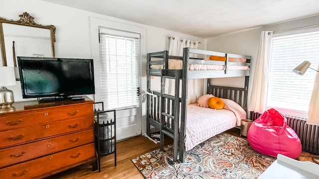 bedroom with radiator heating unit, multiple windows, and wood-type flooring