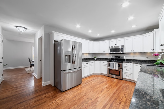 kitchen with dark stone counters, white cabinets, sink, light hardwood / wood-style flooring, and stainless steel appliances