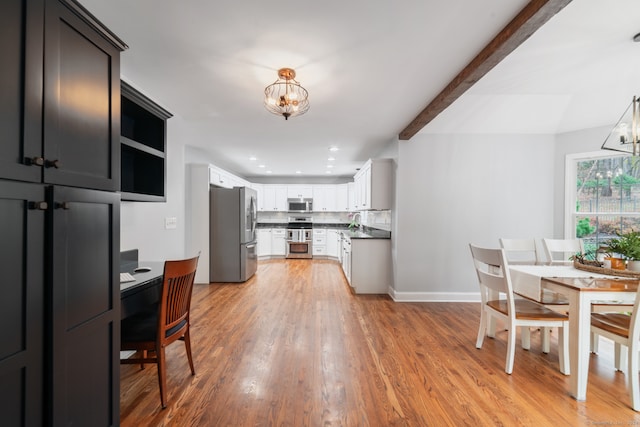 kitchen with beam ceiling, appliances with stainless steel finishes, light hardwood / wood-style floors, white cabinetry, and a chandelier