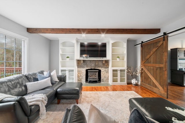 living room featuring beam ceiling, a wood stove, light hardwood / wood-style floors, and a barn door