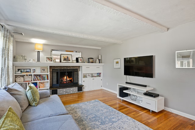 living room featuring a textured ceiling, a brick fireplace, beam ceiling, and hardwood / wood-style flooring