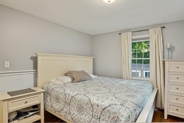 bedroom with dark wood-style floors and a wainscoted wall