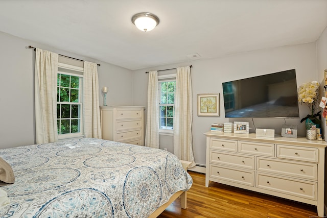 bedroom with a baseboard heating unit and dark wood finished floors