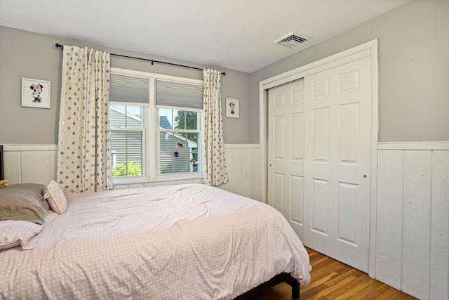 bedroom featuring a closet, a wainscoted wall, visible vents, and wood finished floors