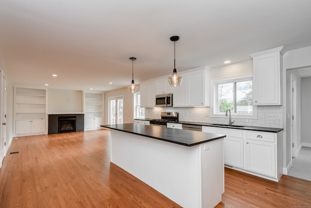 kitchen with stainless steel appliances, white cabinets, sink, hanging light fixtures, and light hardwood / wood-style floors