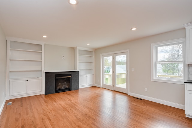 unfurnished living room with built in shelves and light wood-type flooring