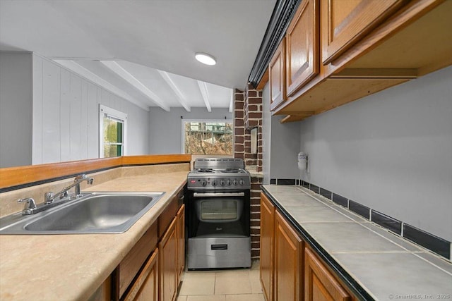 kitchen featuring sink, light tile patterned flooring, stainless steel range with gas stovetop, wooden walls, and beamed ceiling