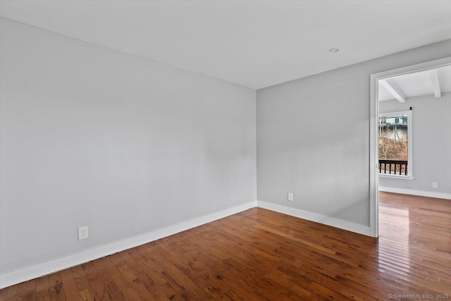 empty room featuring wood-type flooring and beamed ceiling