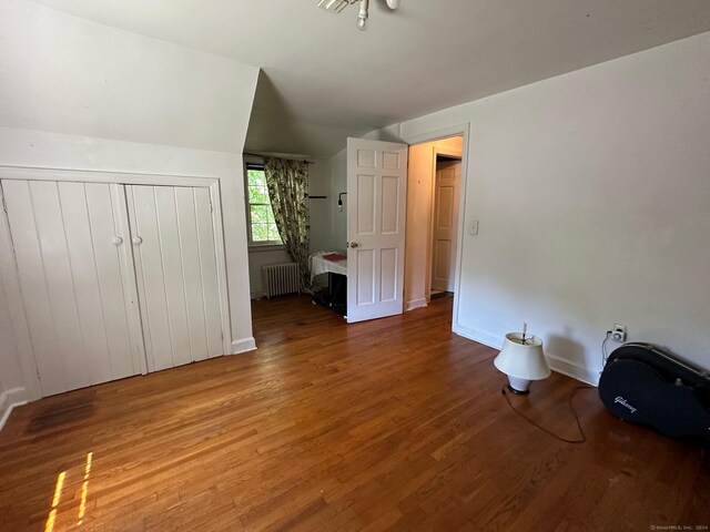 unfurnished bedroom featuring hardwood / wood-style flooring, vaulted ceiling, a closet, and radiator heating unit