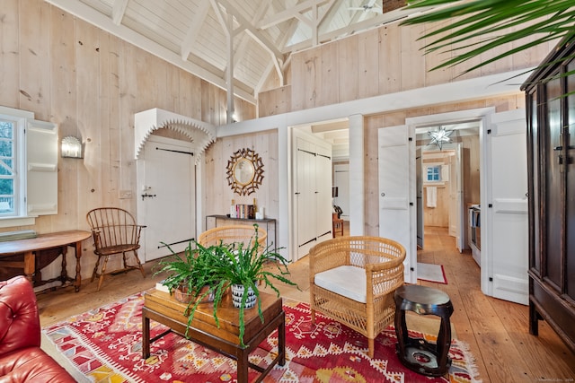 living room featuring wood walls, high vaulted ceiling, wood-type flooring, and ceiling fan