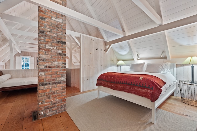 bedroom featuring lofted ceiling with beams, wooden walls, and light hardwood / wood-style floors