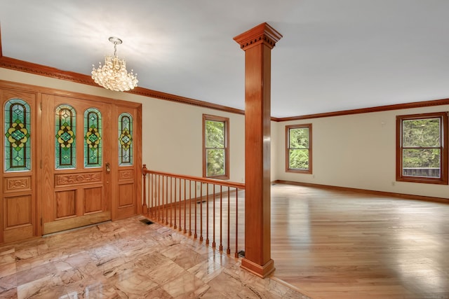 foyer entrance with ornamental molding, a chandelier, and decorative columns