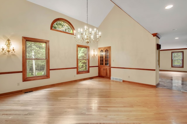 empty room featuring a notable chandelier, high vaulted ceiling, and light wood-type flooring