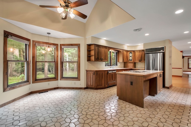 kitchen featuring stainless steel refrigerator, ceiling fan, a center island, tasteful backsplash, and decorative light fixtures