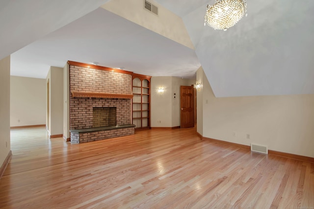 unfurnished living room featuring an inviting chandelier, a fireplace, vaulted ceiling, and light hardwood / wood-style flooring