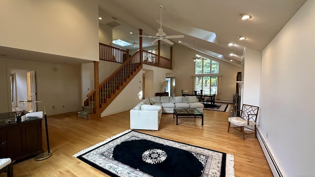 living area with stairs, light wood-style floors, baseboard heating, and high vaulted ceiling