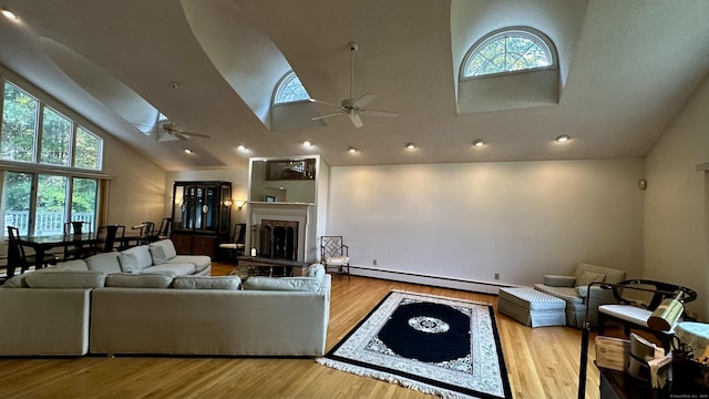 living area with a fireplace with raised hearth, ceiling fan, a skylight, wood finished floors, and a baseboard radiator