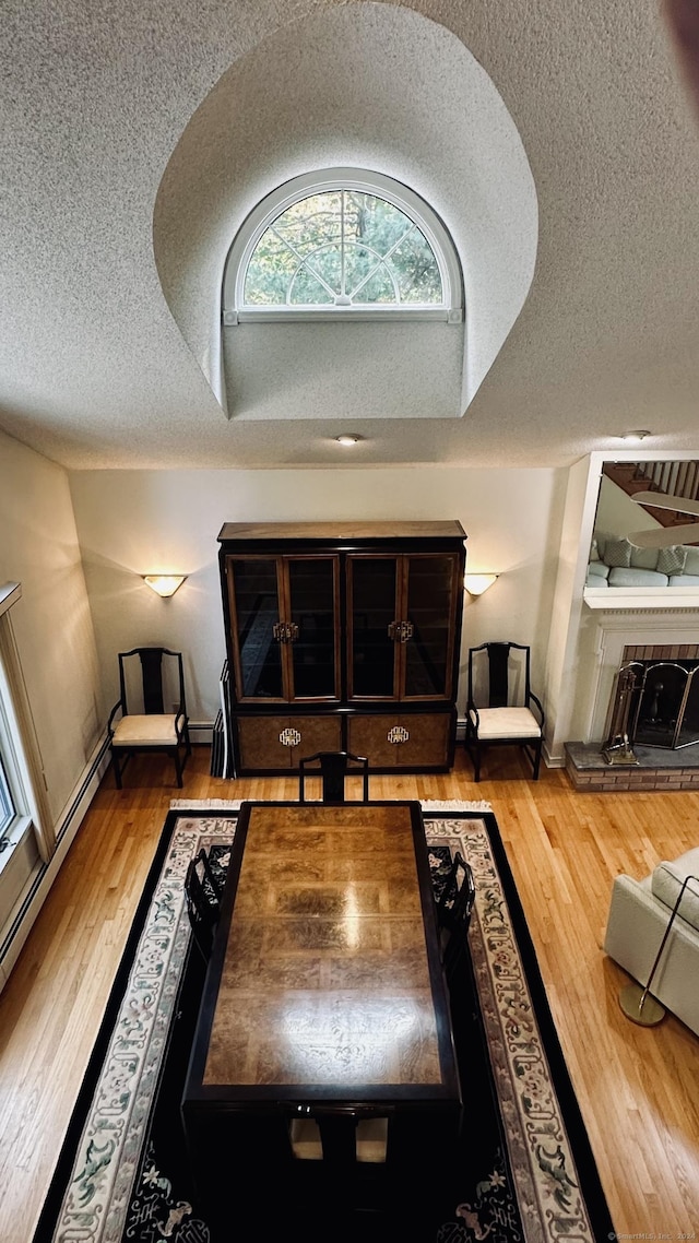 living area featuring vaulted ceiling, a fireplace with raised hearth, a textured ceiling, and wood finished floors