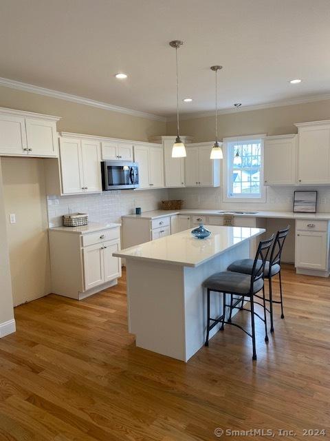 kitchen with white cabinetry, a kitchen island, wood-type flooring, and pendant lighting