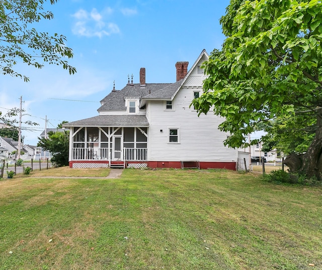 rear view of house featuring a sunroom and a lawn