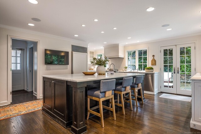 kitchen with dark hardwood / wood-style floors, french doors, ornamental molding, and an island with sink